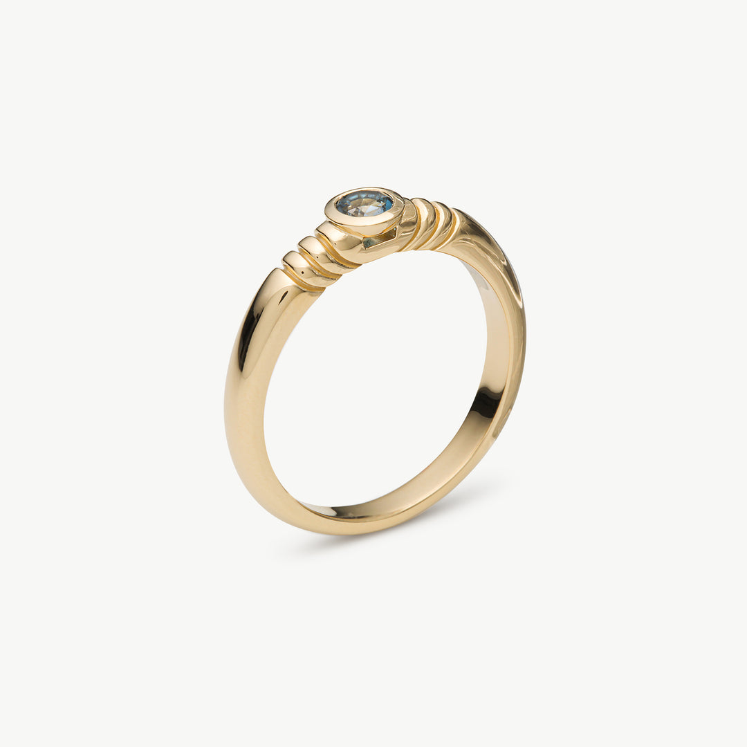 A gold ring with a textured, coiled band detail and a small round clear gemstone, shown on a light gray background.