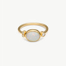 A gold ring featuring an oval white opal center stone and two small clear accent stones, shown on a clean white background.