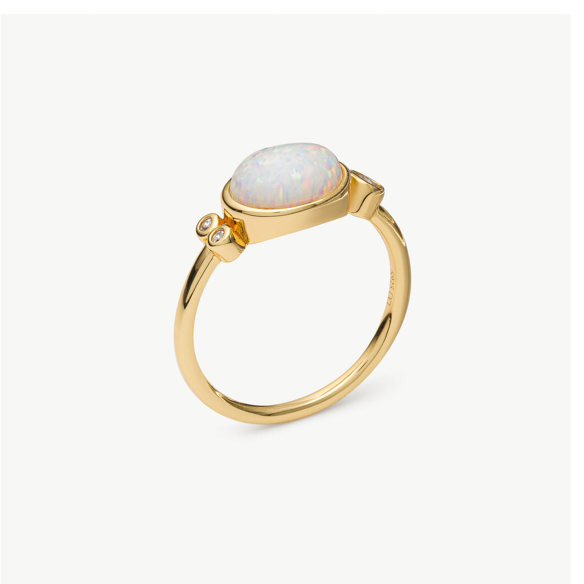 A gold ring featuring an oval cabochon opal with iridescent white, blue, and pink flashes, accented by two small round clear stones on the band, set against a light gray background.