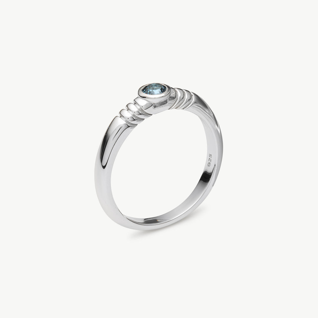 A polished sterling silver ring with a textured twisted band and a small round light blue gemstone, shown on a clean off-white background.