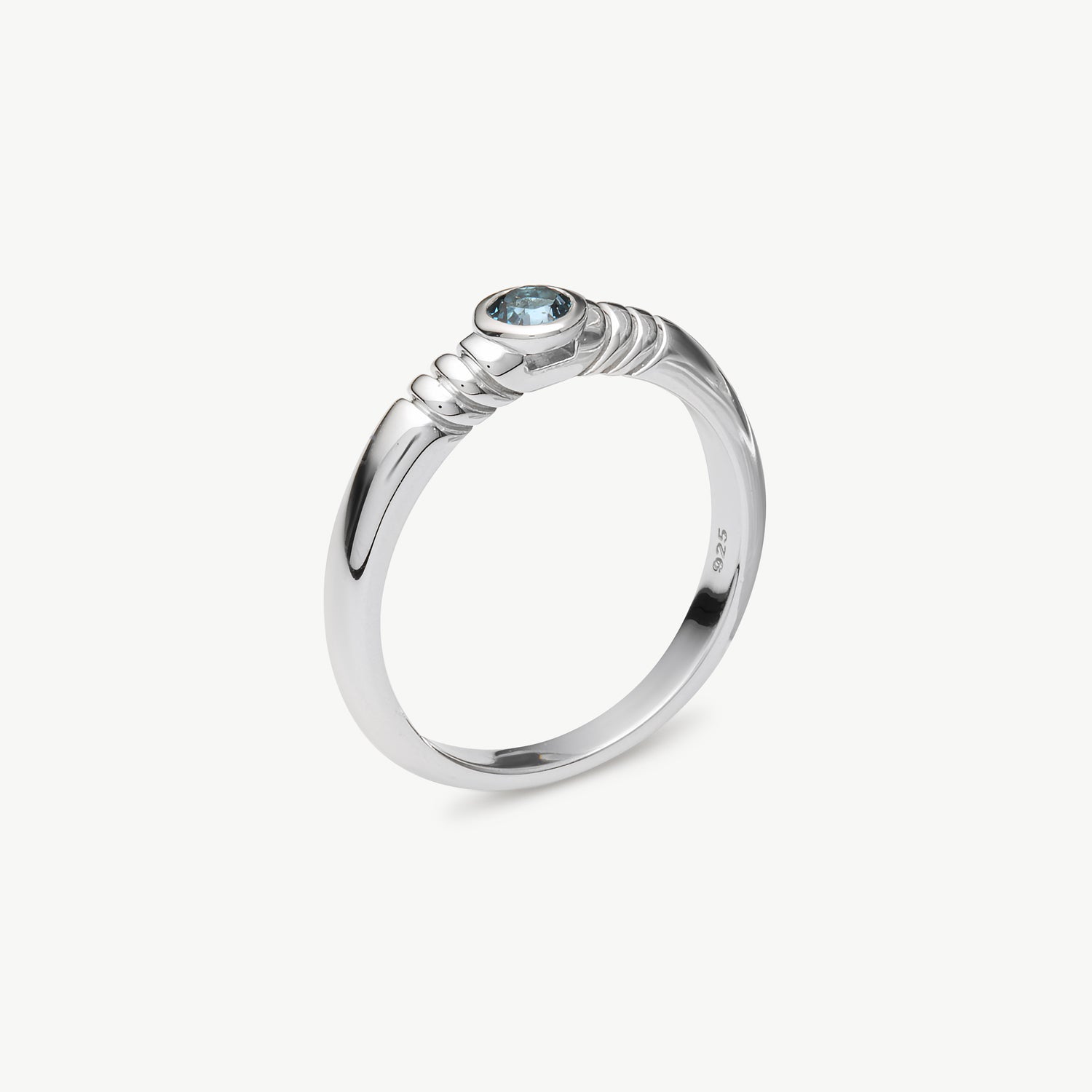 A polished sterling silver ring with a textured twisted band and a small round light blue gemstone, shown on a clean off-white background.