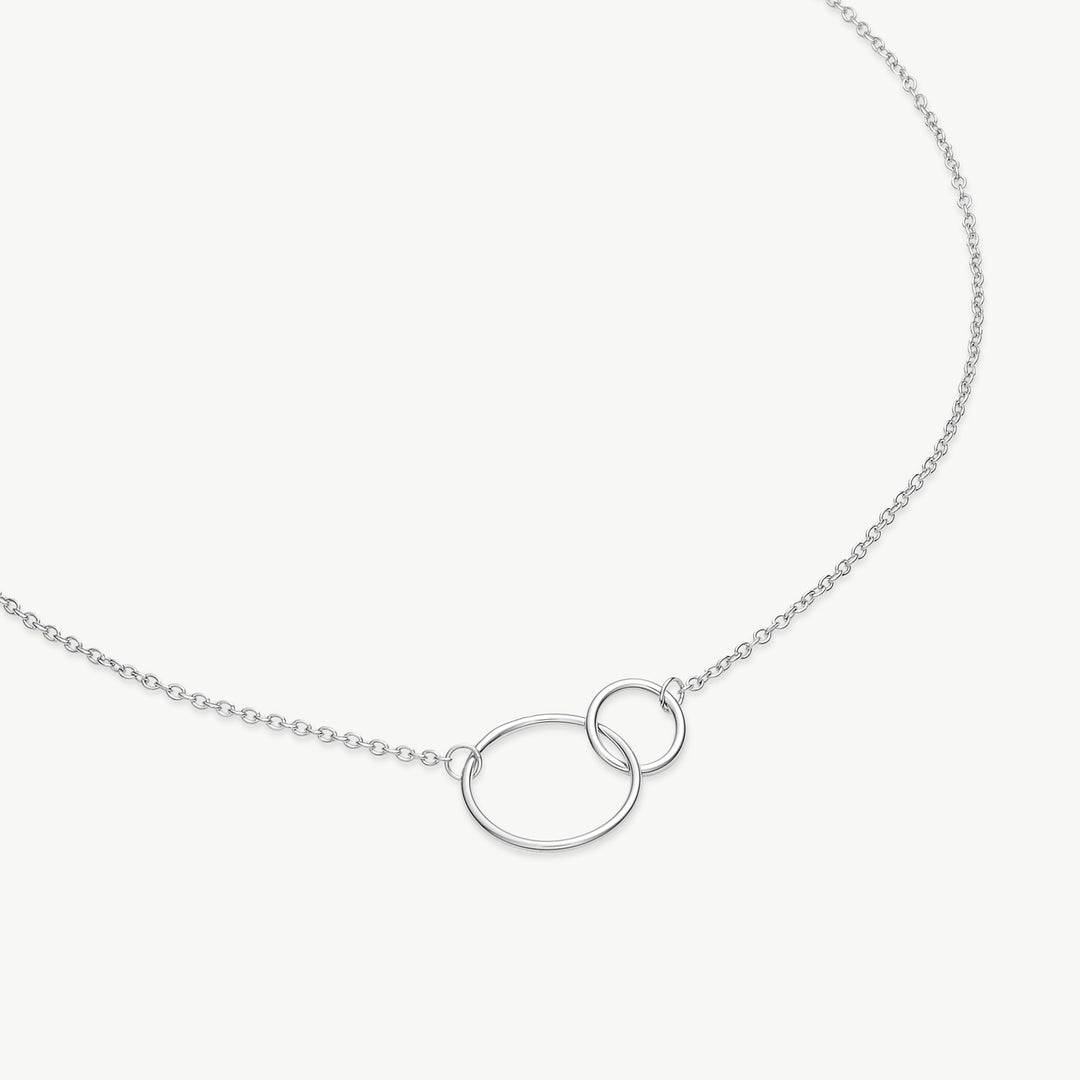 A silver chain necklace featuring two interlocking oval links at the center, displayed on a clean, light off-white background.