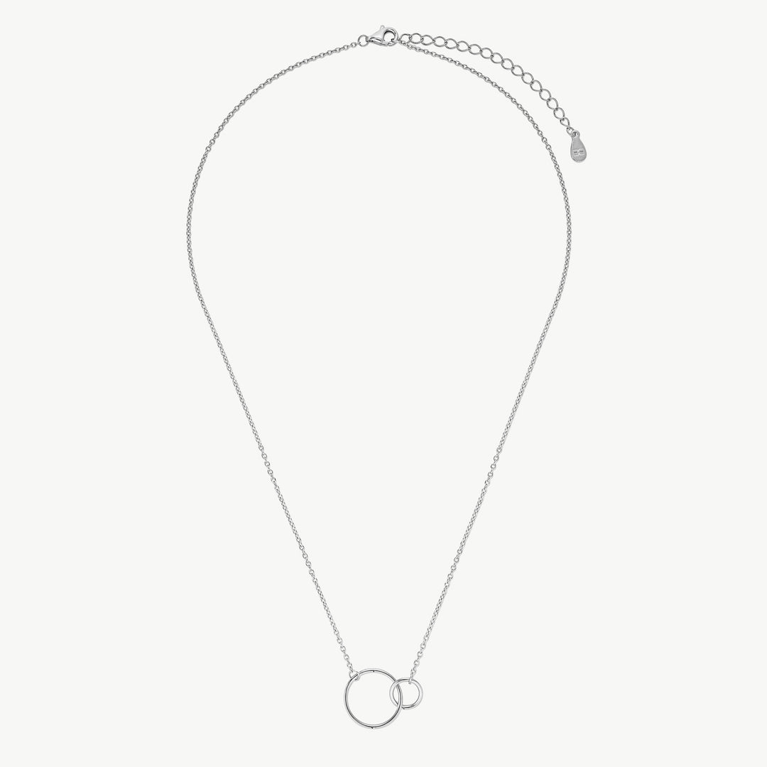 A silver chain necklace with two interlocking minimalist circular pendants, displayed on a clean, light off-white background.
