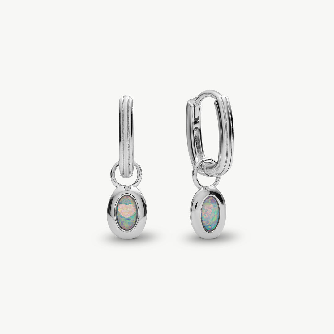 A pair of silver huggie hoop earrings with oval opal inlays, shown on a clean off-white background.
