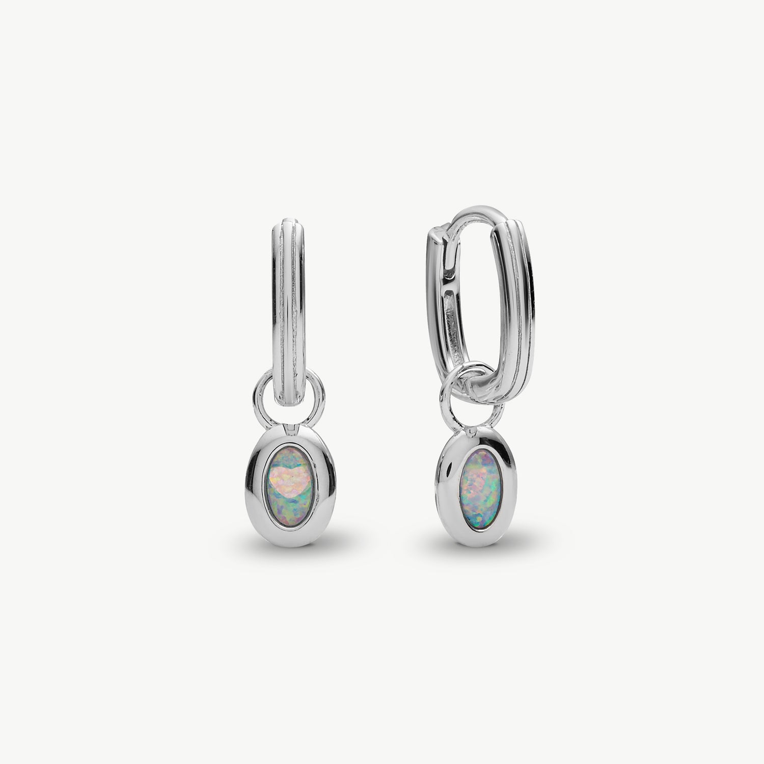 A pair of silver huggie hoop earrings with oval opal inlays, shown on a clean off-white background.