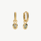 A pair of gold huggie hoop earrings with oval opal gemstone charms, displayed on a clean off-white background.