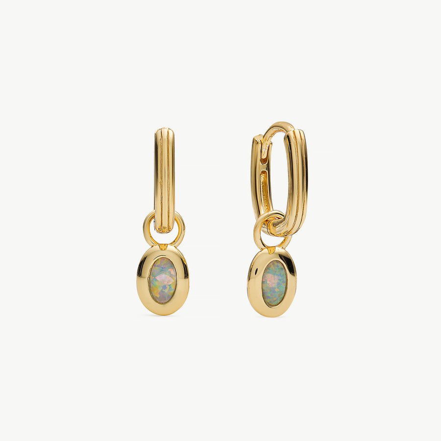 A pair of gold huggie hoop earrings with oval opal gemstone charms, displayed on a clean off-white background.