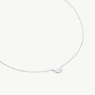 A delicate silver chain necklace featuring a small, fan-shaped shell pendant, displayed against a clean, light off-white background.
