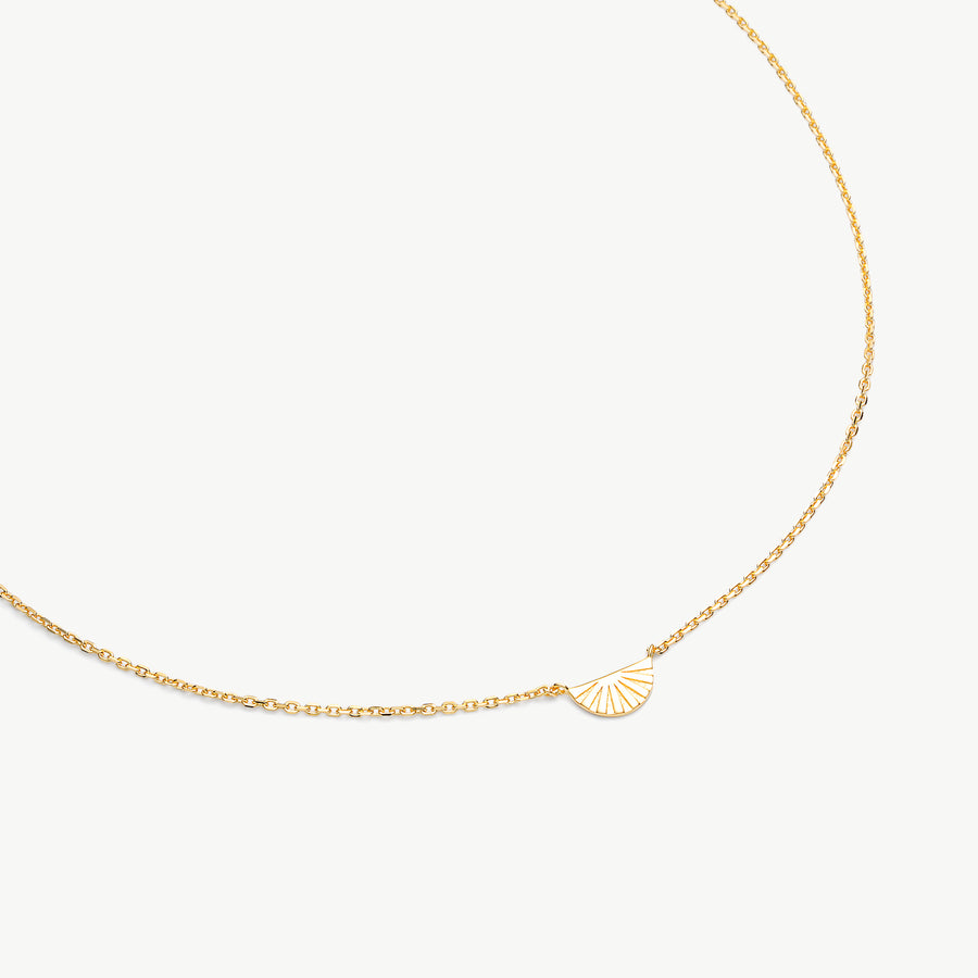 A delicate gold chain necklace featuring a small, minimalist fan-shaped pendant with radiating lines, displayed on a clean off-white background.