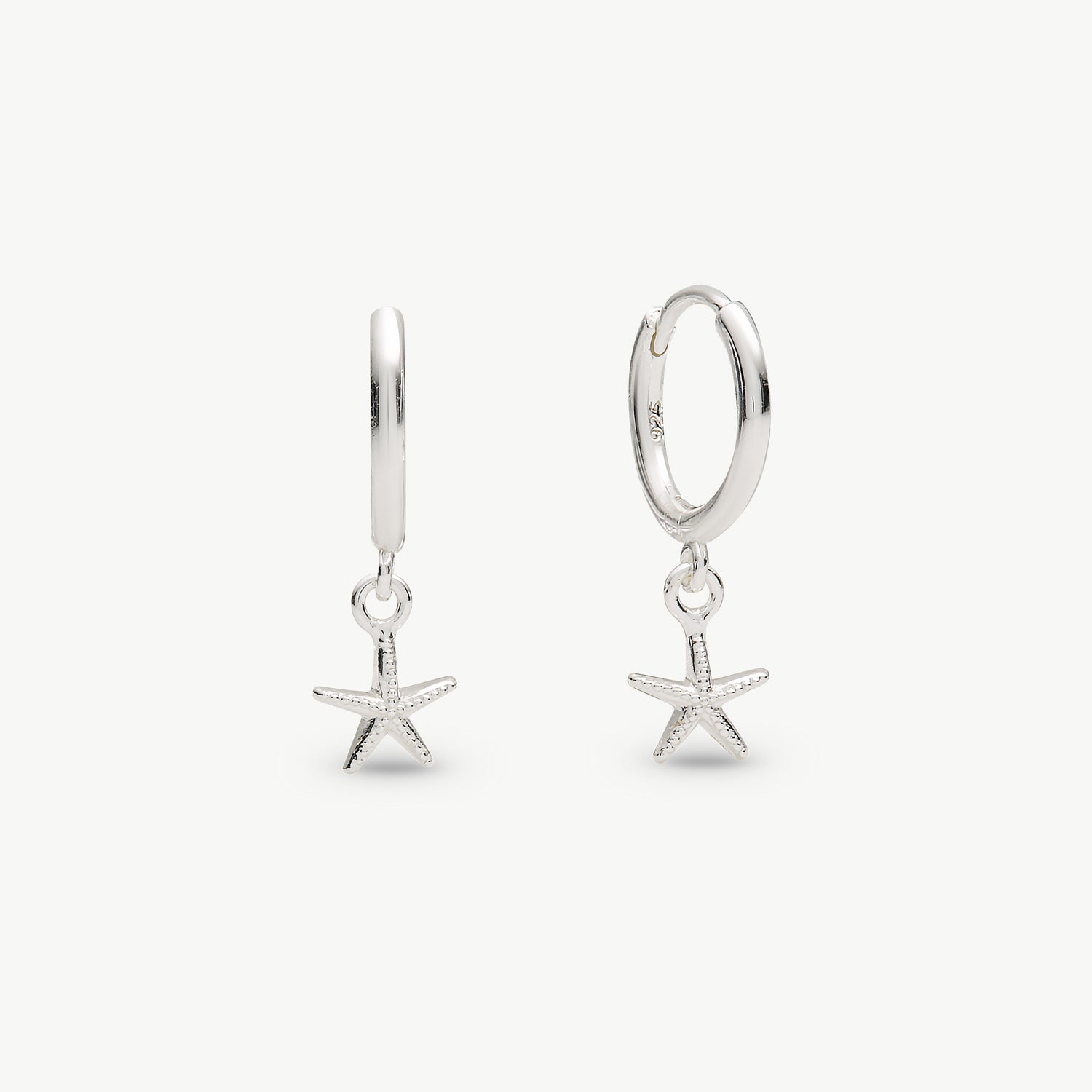 A pair of silver huggie hoop earrings with dangling starfish charms, shown on a clean off-white background.
