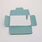 A white microfiber cloth with black 'BOWE' branding, neatly folded inside an open light blue cardboard presentation box on a clean white background.