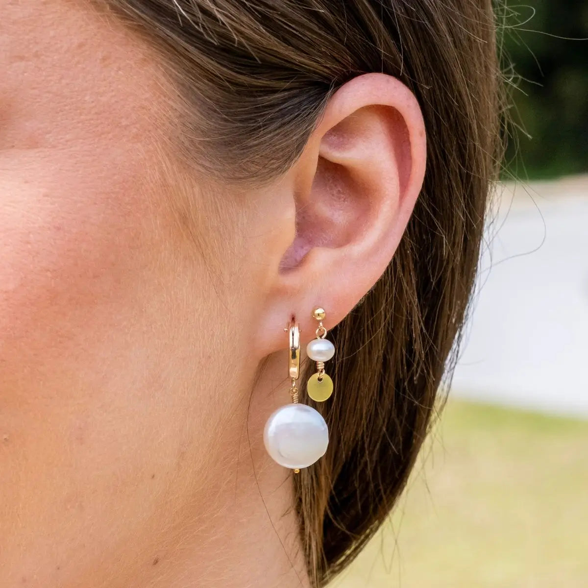Close-up of an ear wearing gold and pearl earrings with blurred background