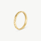 A gold band ring with a textured, openwork geometric pattern on the outer surface, shown on a light gray background.