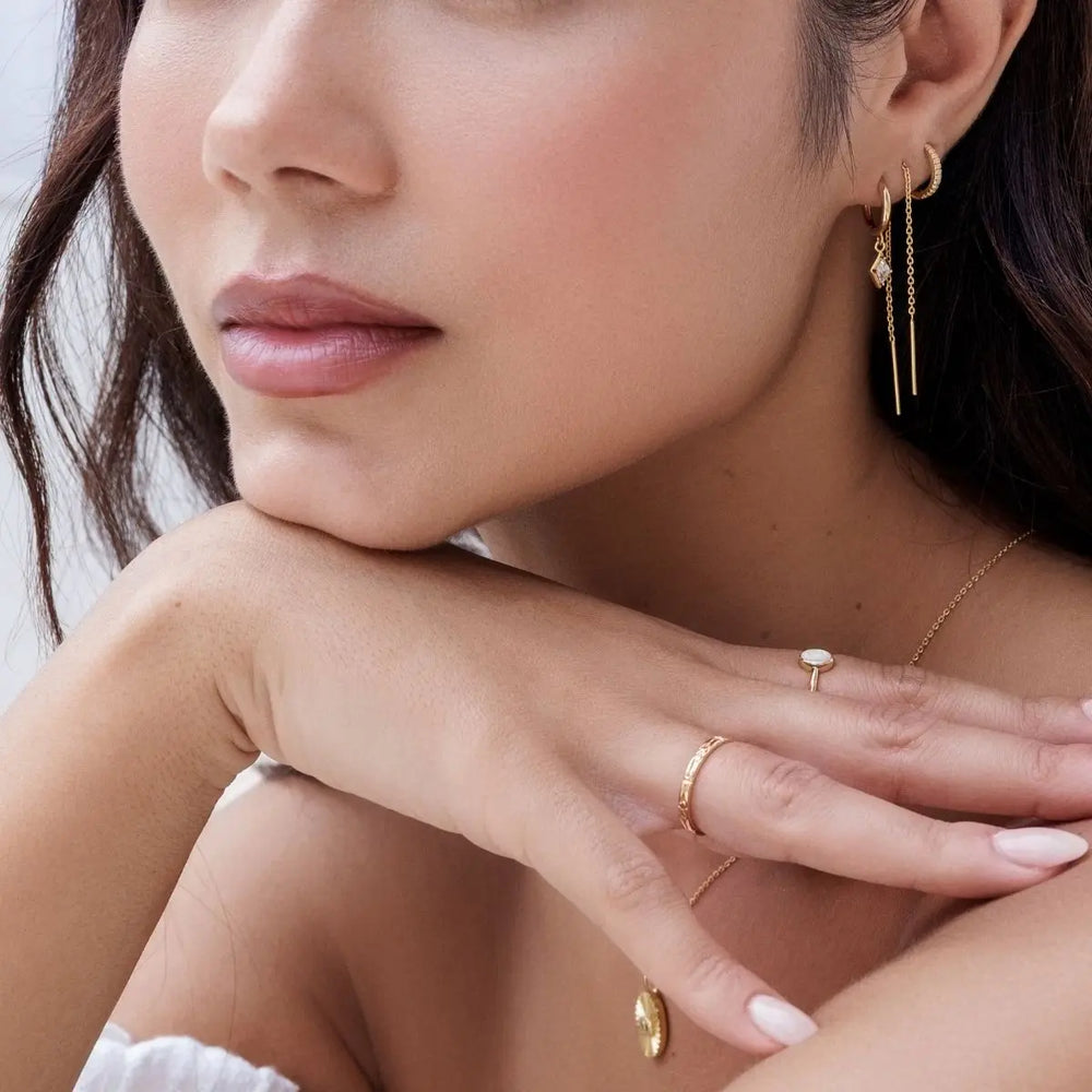 Close-up of a woman wearing gold jewelry including earrings, rings, and a necklace.