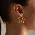 A close-up of a model's ear wearing a delicate gold hoop earring with a small, openwork butterfly or flower-like motif.