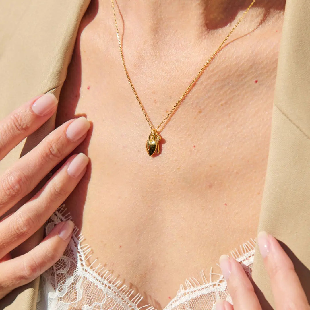 Gold necklace with a pendant on a person wearing a beige top and white lace garment.