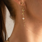 A close-up of a model's ear and neck wearing a gold dangle earring with starfish, shell, and pearl details.