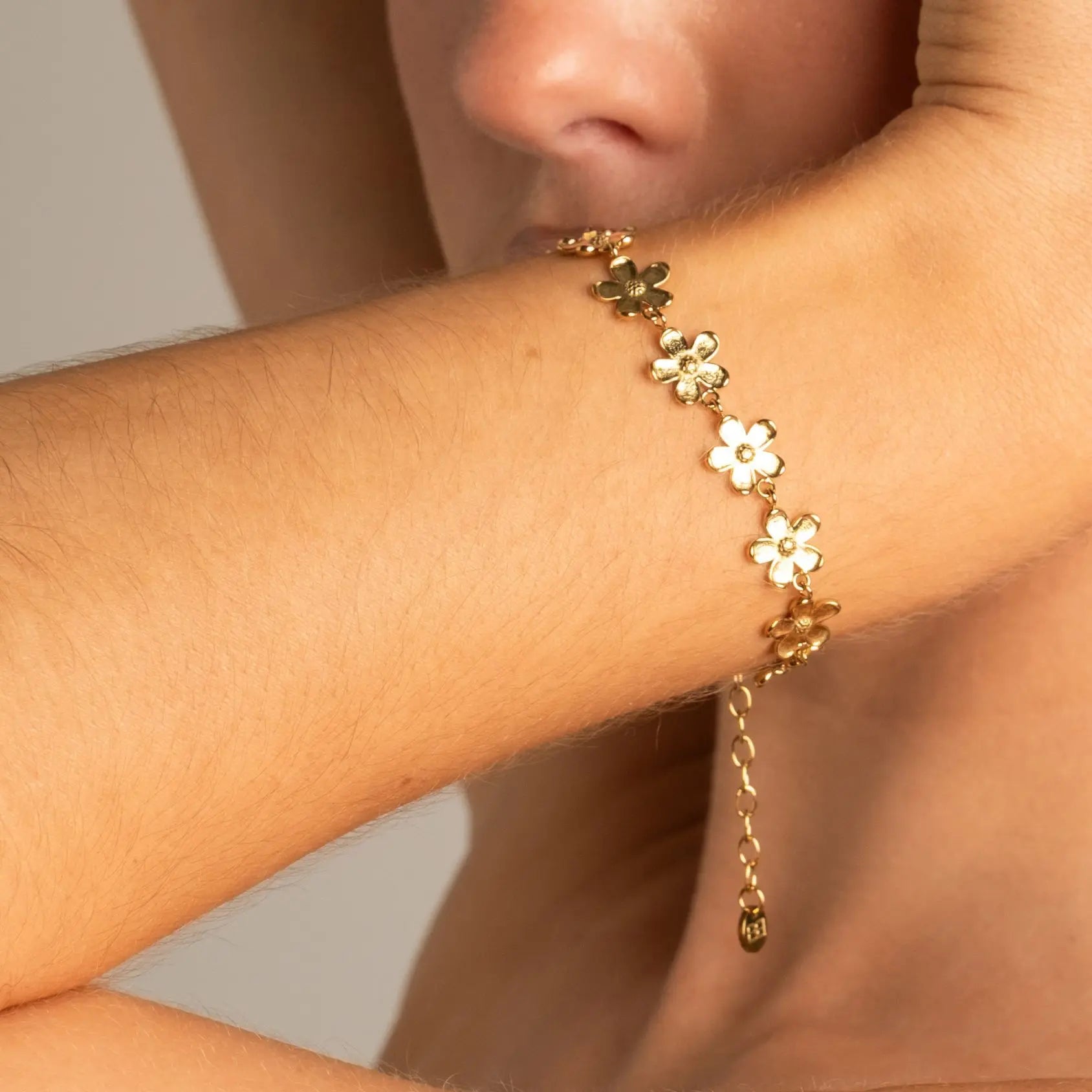 A gold chain bracelet with five flower charms, featuring alternating white and gold blossoms, worn on a person's wrist.