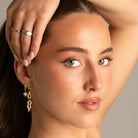 Picture of a girl wearing two rings, looking at the camera, and two long dangling earrings on a grey background 