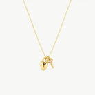 Hanging gold lock with key necklace suspended from chain against a cream background 