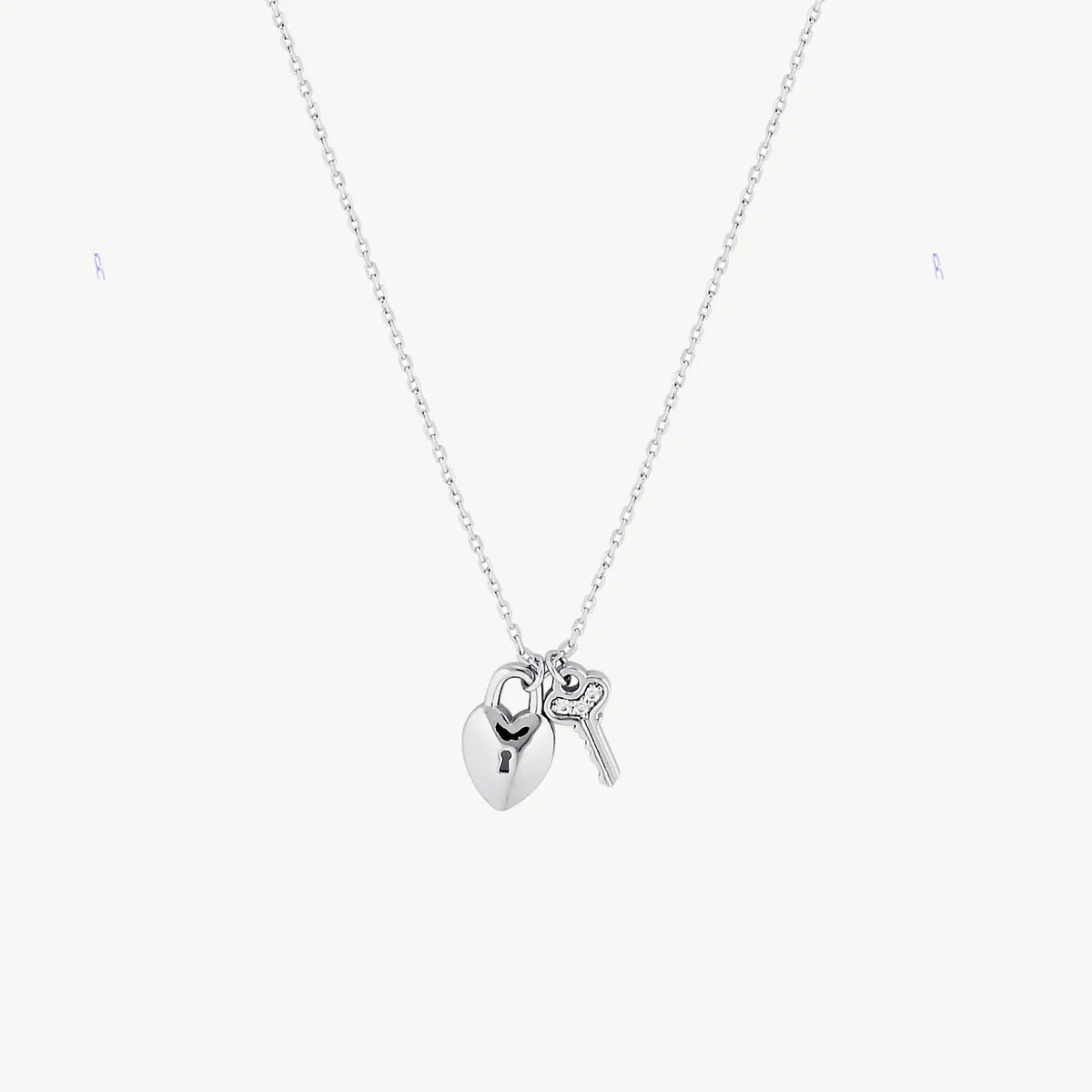 Hanging silver lock necklace with key charm suspended from silver chain against a cream background 