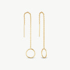 A pair of gold dangle earrings on a light off-white background. Each earring features a delicate chain leading to a large open circular pendant, one in a vertical oval orientation and the other in a horizontal oval orientation.