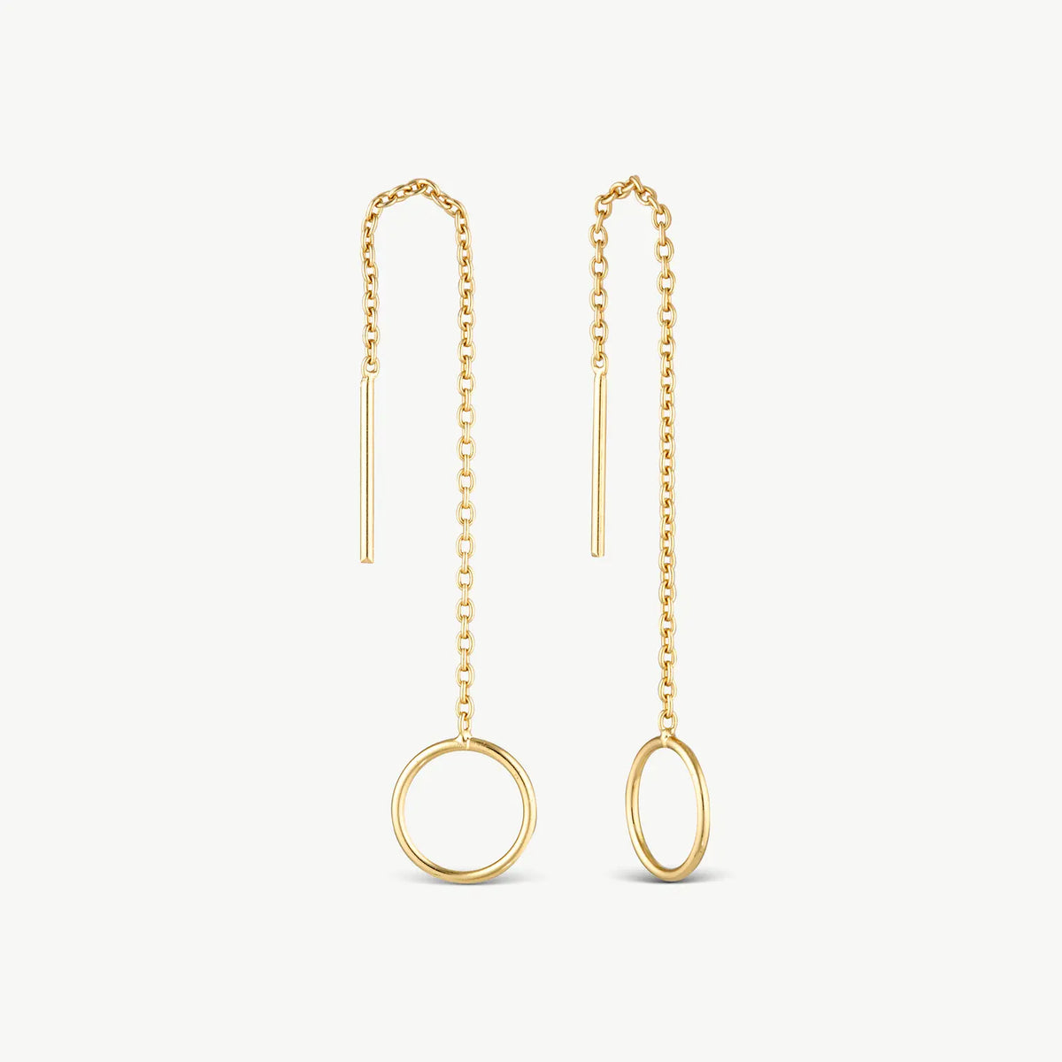 A pair of gold dangle earrings on a light off-white background. Each earring features a delicate chain leading to a large open circular pendant, one in a vertical oval orientation and the other in a horizontal oval orientation.