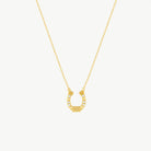 A yellow gold hanging horseshoe charm suspended from a fine gold cable chain with sparkling cubic zirconias on a cream background 