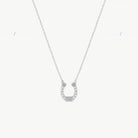 A hanging silver horseshoe charm suspended from a fine cable chain with cubic zirconias on a cream background 