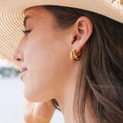 Close-up of a woman wearing gold hoop earrings with a blurred background