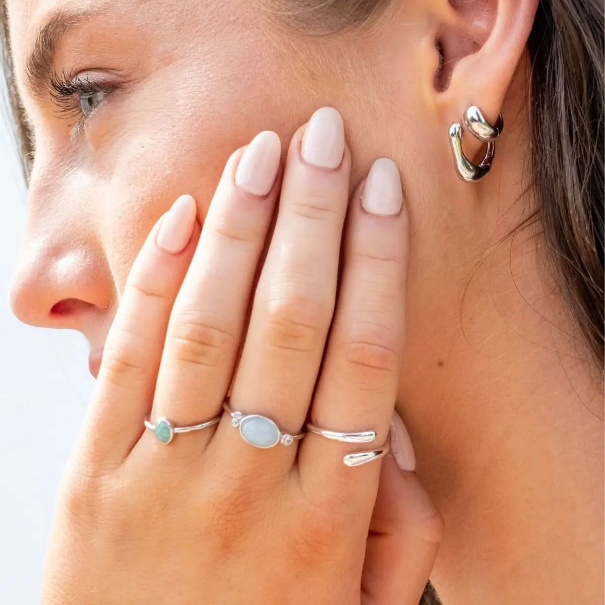 Close-up of a woman wearing silver hoop earrings and multiple rings on a light background