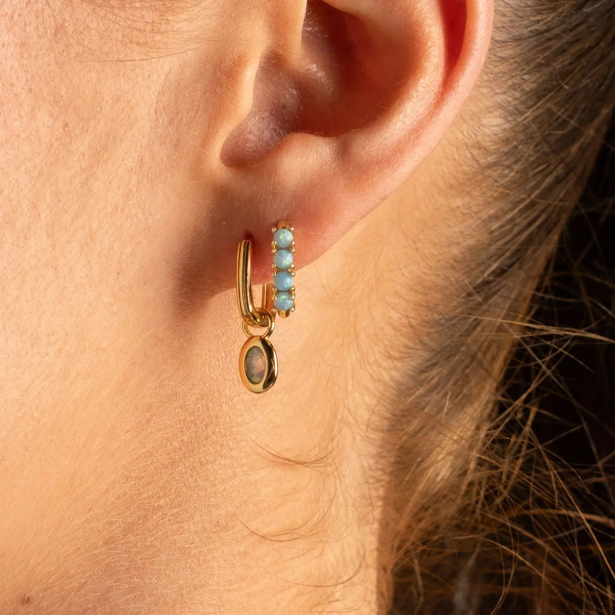 A close-up lifestyle shot of a woman wearing a delicate gold ring with a small oval light blue stone on her finger.