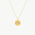 A cubic zirconia-set Evil Eye motif on a radiating fan disc background, suspended from a yellow gold chain on a cream background 