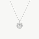 A sparkling Evil Eye motif on a radiating disc background in silver, suspended from a silver chain on a cream background 