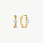A pair of gold huggie hoop earrings, one shown from the front and the other from the side, each featuring a small oval light blue opal stone in a prong setting, on a clean off-white background.