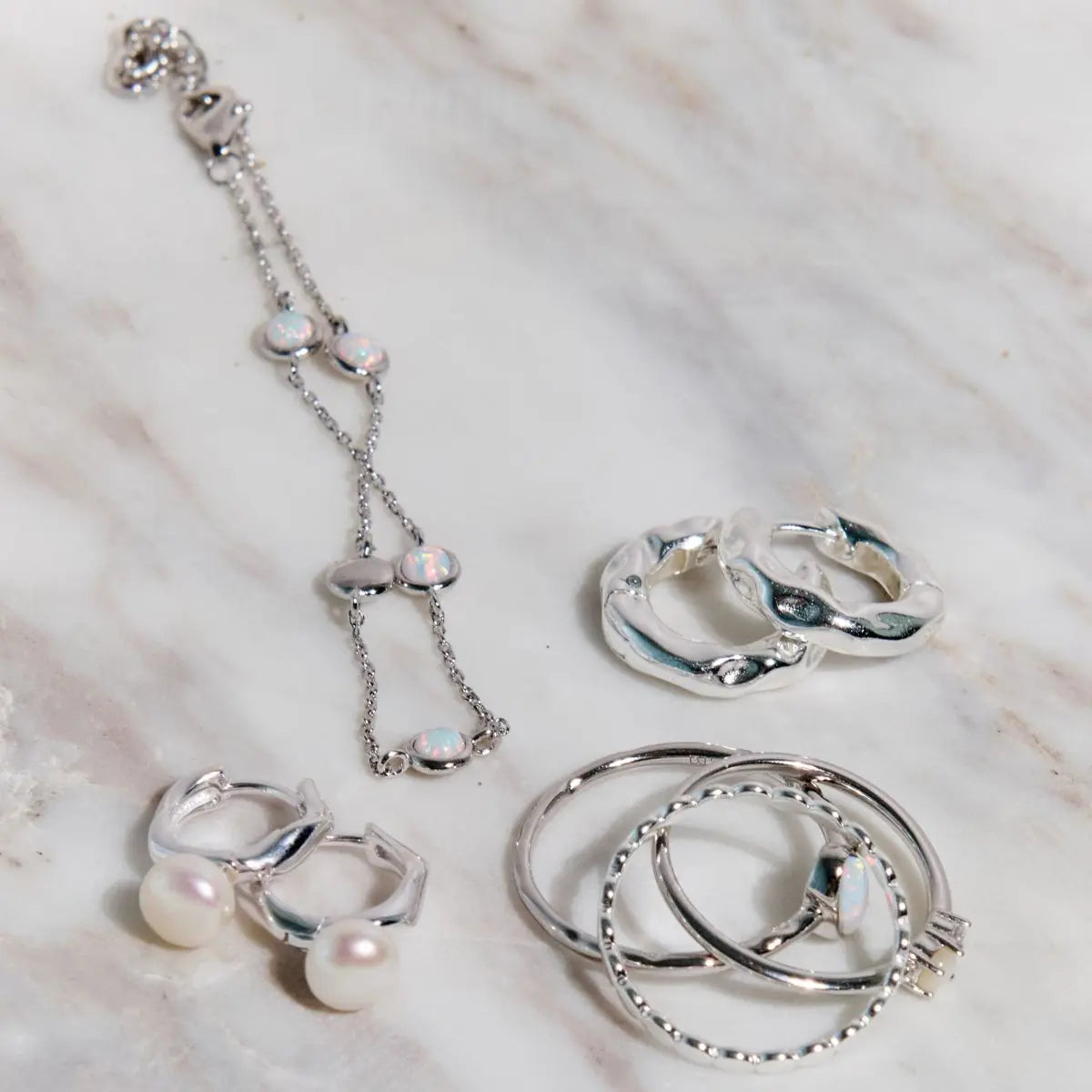 Silver jewelry set including rings and a necklace on a textured surface