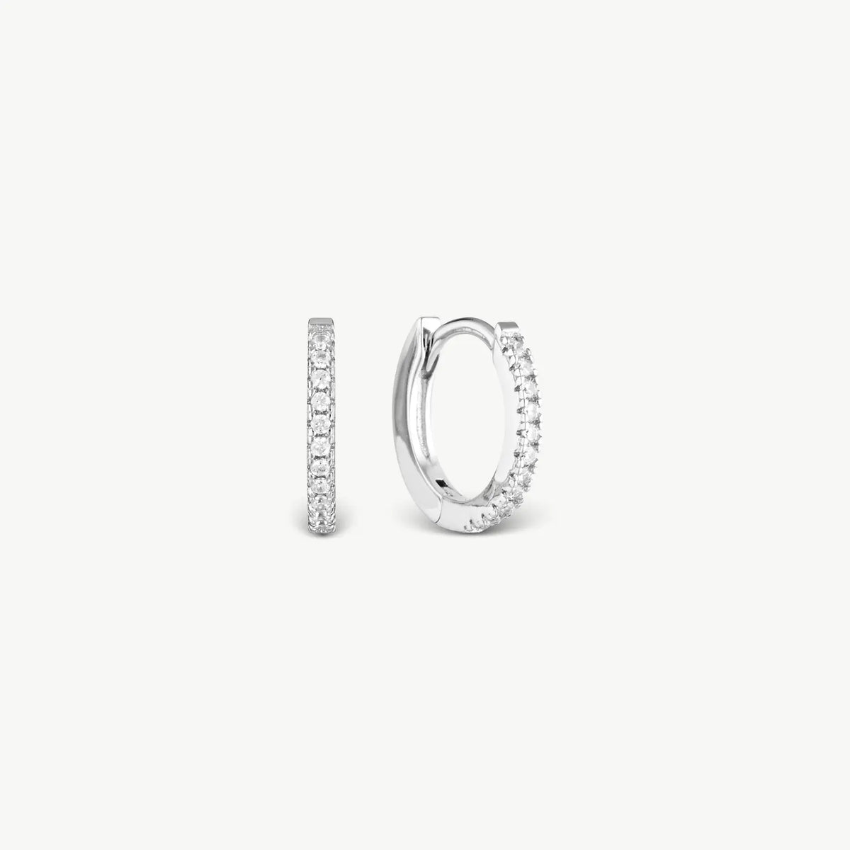 A pair of small silver huggie hoop earrings with clear pavé stones, shown from side and back views on a light gray background.