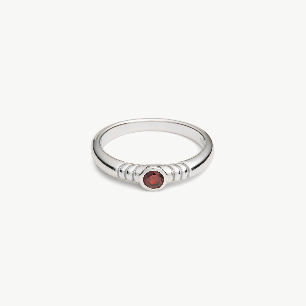 A silver ring with a textured beaded band and a small round red gemstone in the center, shown on a plain light gray background.