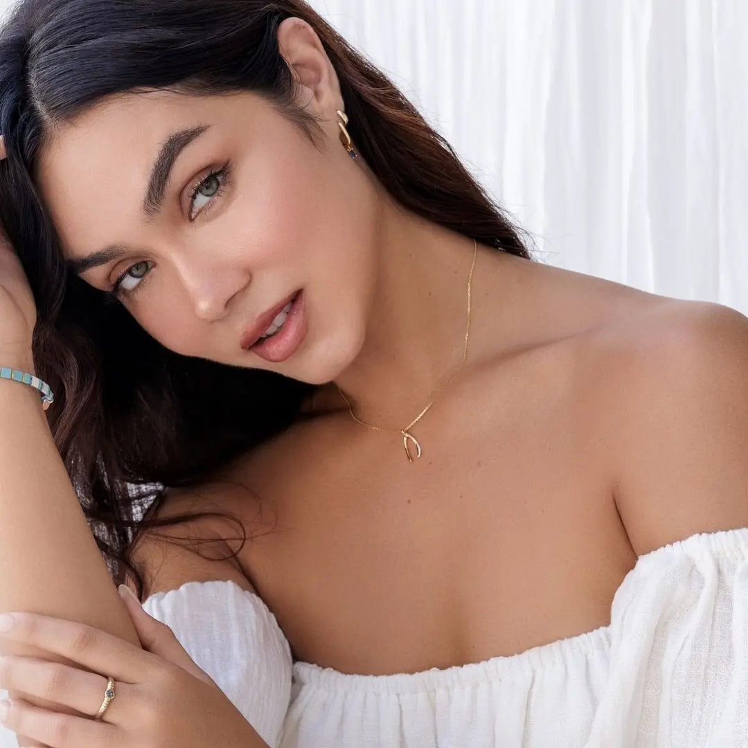 Woman wearing a gold necklace and white top with a blurred background