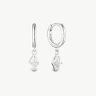 A pair of silver huggie hoop earrings with dangling diamond-shaped clear gemstone charms, shown on a light gray background.