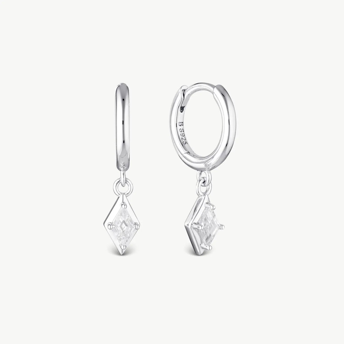 A pair of silver huggie hoop earrings with dangling diamond-shaped clear gemstone charms, shown on a light gray background.