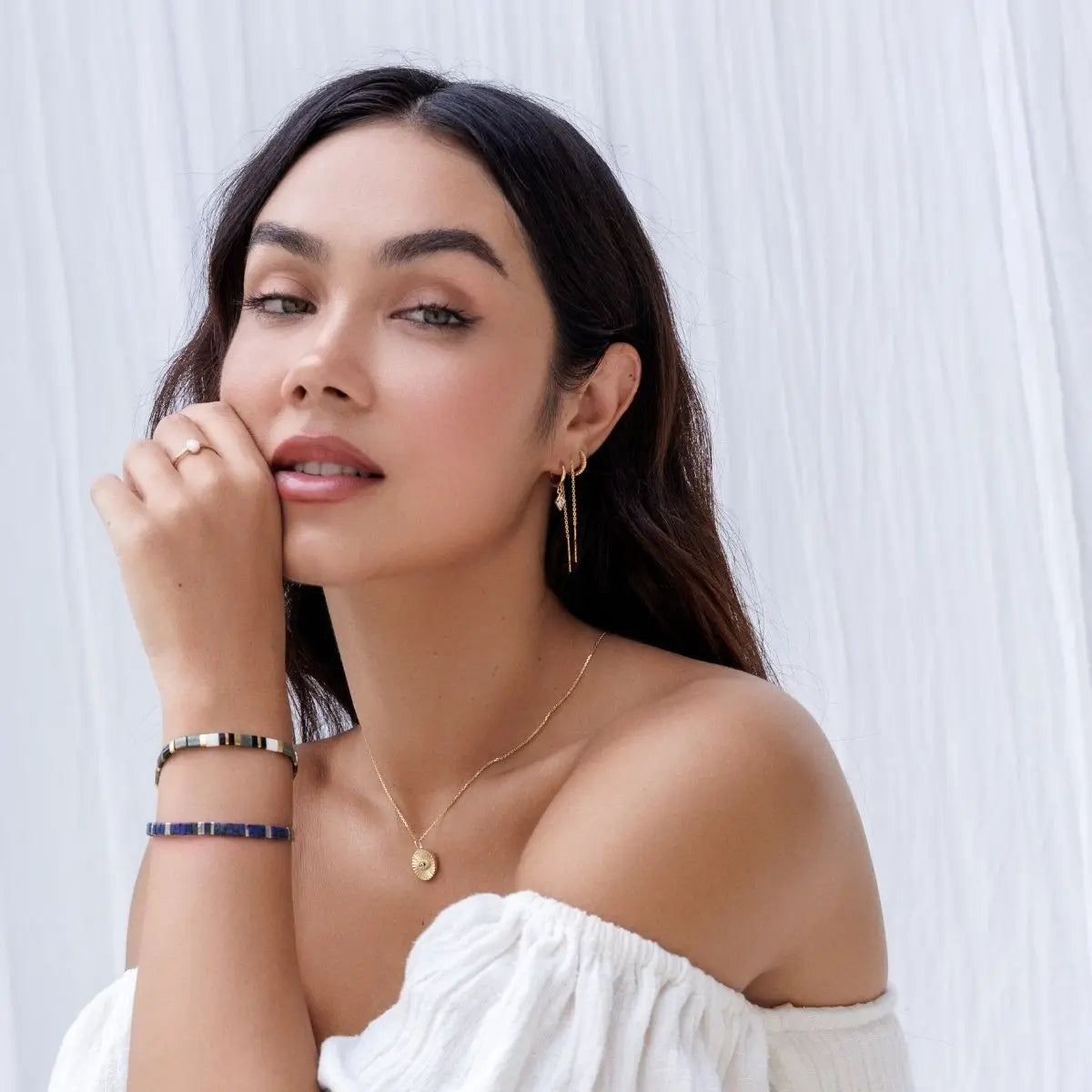 Woman wearing gold jewelry including a necklace, earrings, and bracelets against a white background