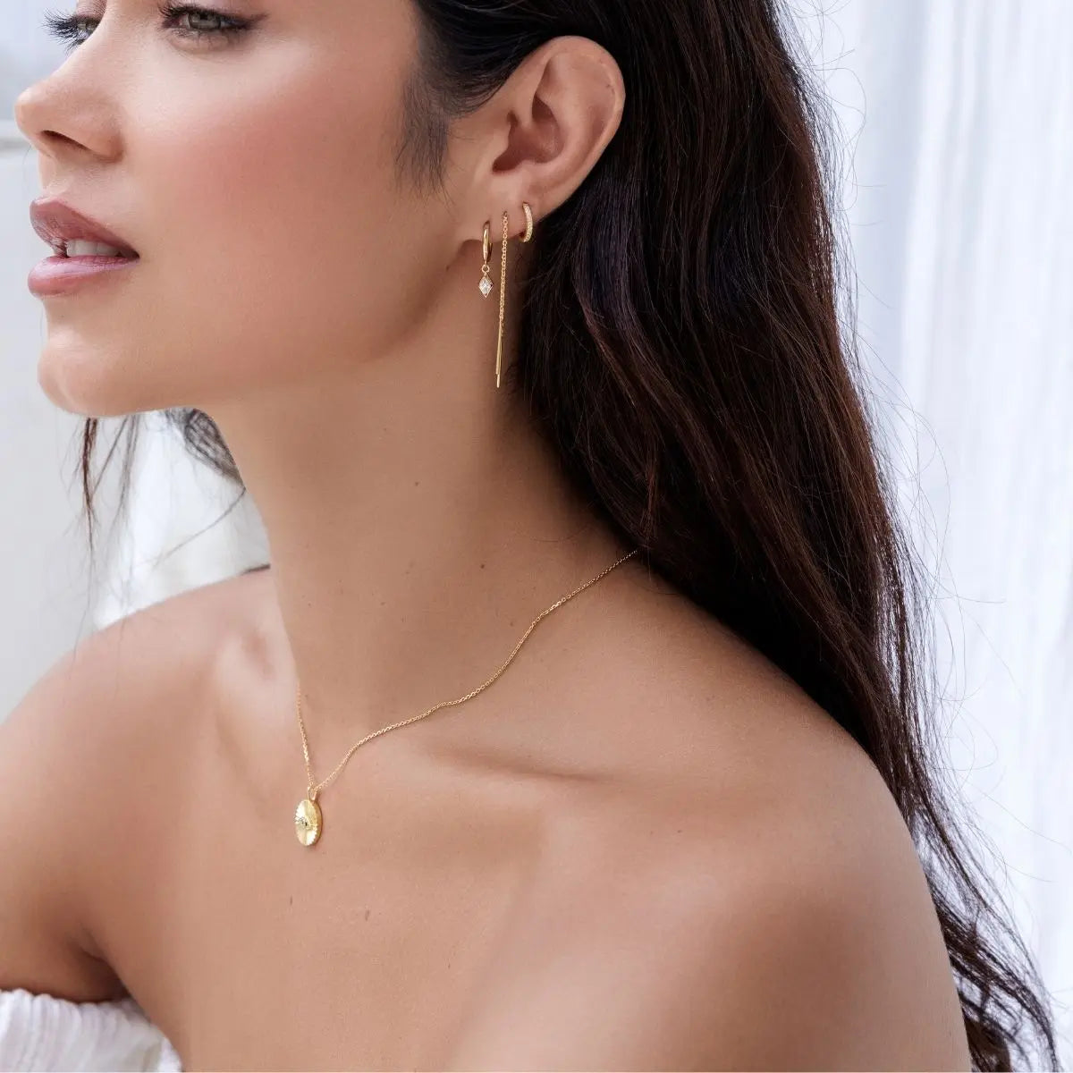 Close-up of a woman wearing gold earrings and necklace against a white background