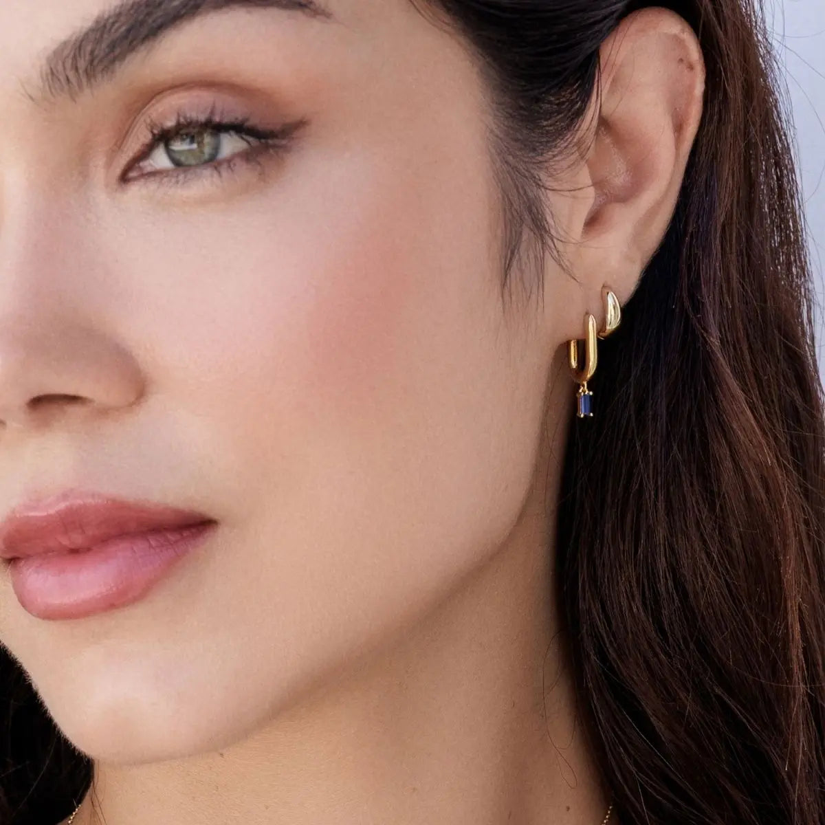 Close-up of a woman wearing gold hoop earrings with a blue gemstone.