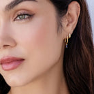 Close-up of a woman wearing gold hoop earrings with a blue gemstone.