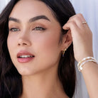 Woman wearing gold earrings and bracelets with a neutral background
