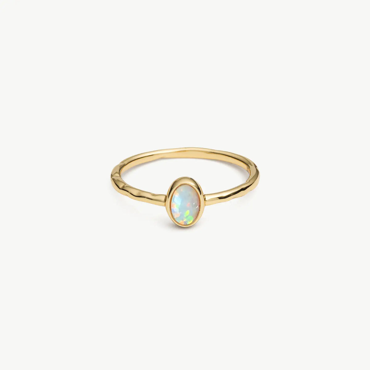 A delicate gold ring featuring a small oval cabochon opal stone in a bezel setting, shown on a clean off-white background.