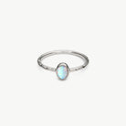 A silver ring featuring a small oval opal gemstone with iridescent white, blue, and green play-of-color, set against a clean off-white background.