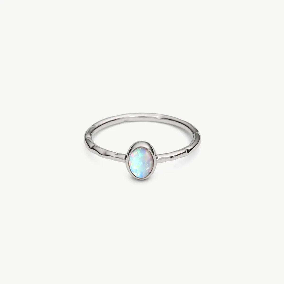 A silver ring featuring a small oval opal gemstone with iridescent white, blue, and green play-of-color, set against a clean off-white background.