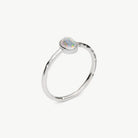 A silver ring featuring a small, oval-shaped iridescent opal gemstone in a bezel setting, shown on a clean off-white background.